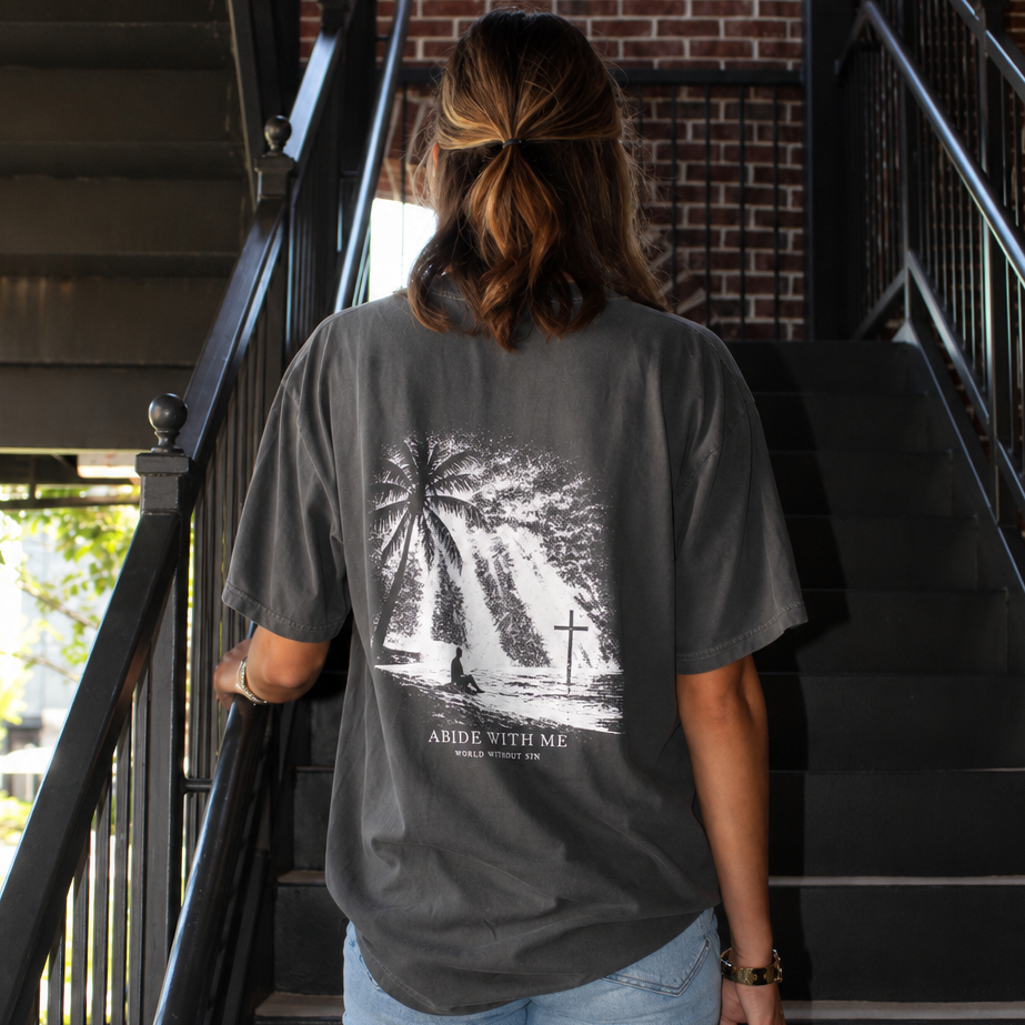 A woman viewed from behind wearing a dark gray graphic t-shirt and light blue jeans, walking up an outdoor black metal staircase next to a brick building.